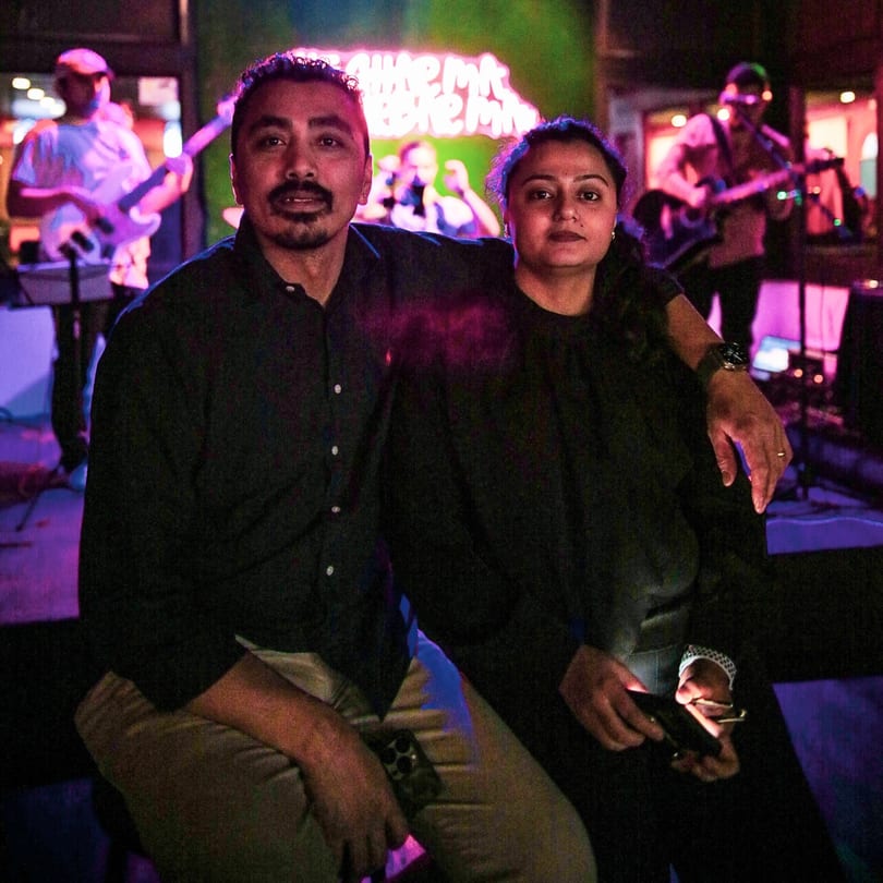 A man and woman sit in a dimly lit restaurant with musicians playing in the background.