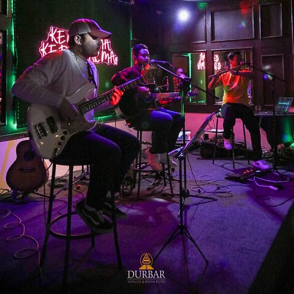 Three musicians performing live on stage with neon lights in a dark room at Durbar Bistro.
