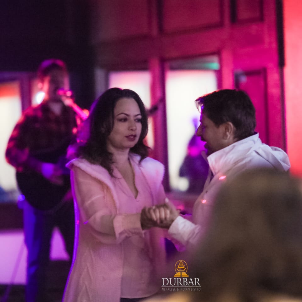 A couple dancing under purple and pink lights, with a musician playing guitar in the background.