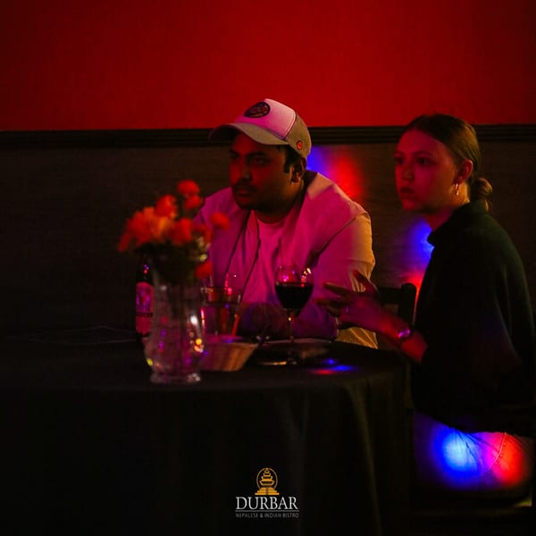Two patrons at Durbar Nepalese and Indian Bistro, enjoying drinks in a dimly lit, red-hued setting.