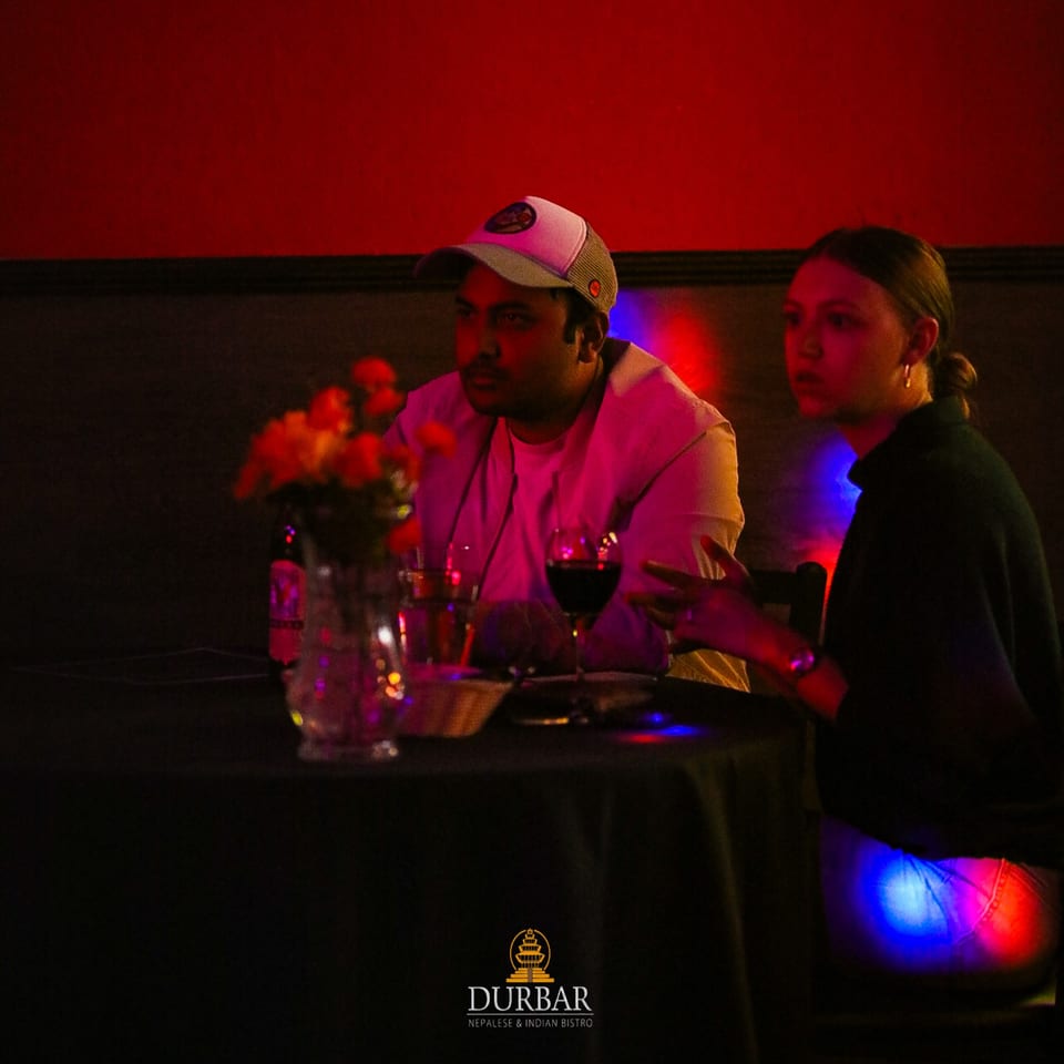 Two patrons at Durbar Nepalese and Indian Bistro, enjoying drinks in a dimly lit, red-hued setting.